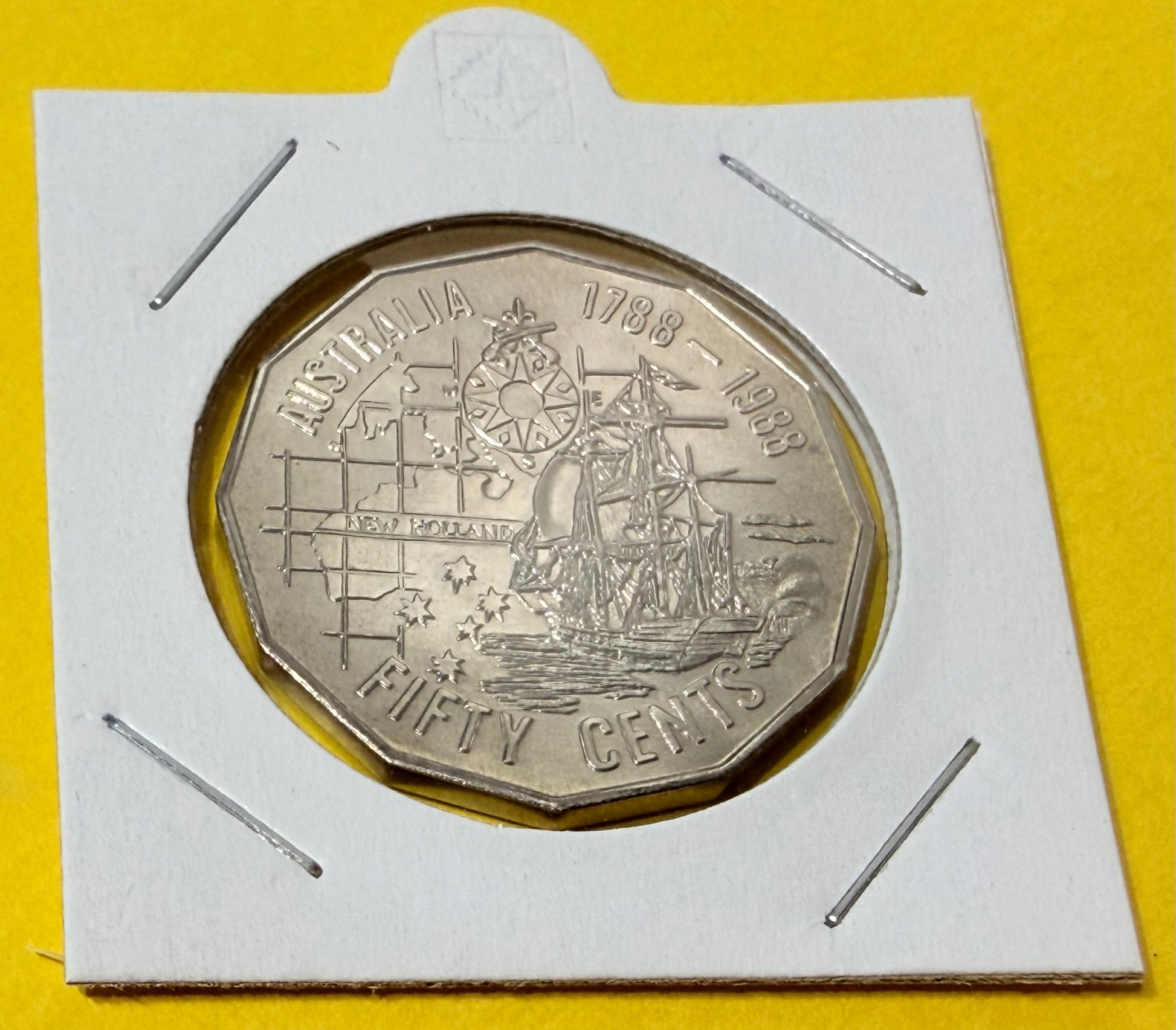 Silver coin with 'Australia' and 'Fifty Cents' text on a white card against a yellow background