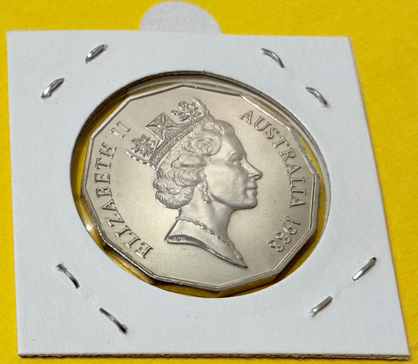 Silver coin with a profile of a queen on a white card against a yellow background