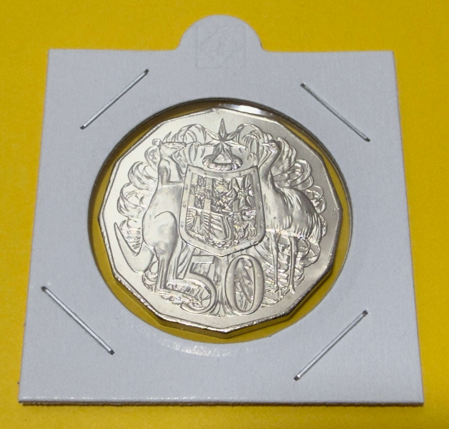 Silver coin with a design on a white card against a yellow background