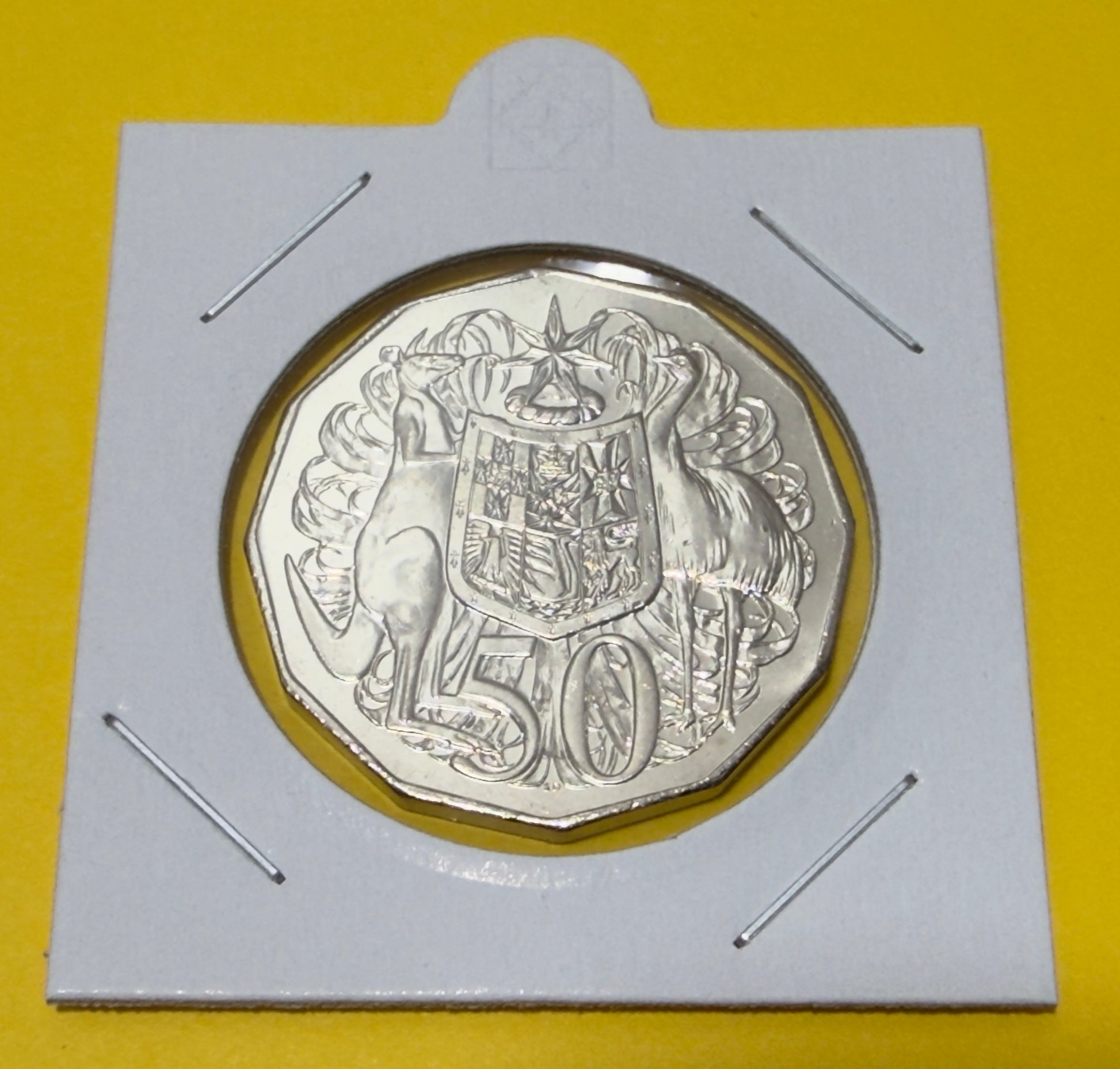 Silver coin with a design on a white card against a yellow background